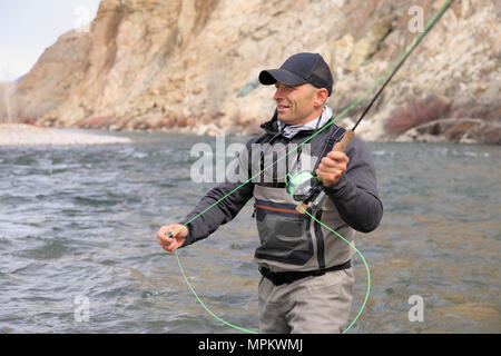 pêcheur adulte de sexe masculin qui se coud à gué et jette une tige de mouche une rivière Banque D'Images