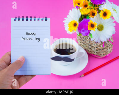 Concept de la fête des pères. Main tenant ne pas réserver avec Happy Father's Day Message sur le carnet de notes avec fleur rose, tasse de café avec une moustache noire sur rose retour Banque D'Images