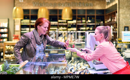Jeune vendeuse au comptoir de produits frais dans le supermarché sert un client - vente de fromage et de la viande Banque D'Images