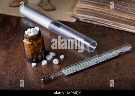 Paquet de pilules bleues avec des ampoules de verre, thermomètre et vieux livre médical. Un tube à essai avec médicament. Banque D'Images