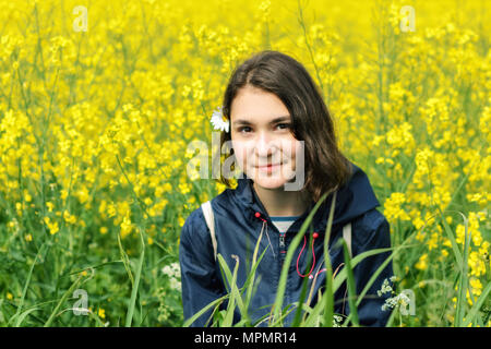 Une adolescente dans une veste bleue et de la camomille dans ses cheveux, se trouve dans un domaine parmi les fleurs jaunes. Banque D'Images