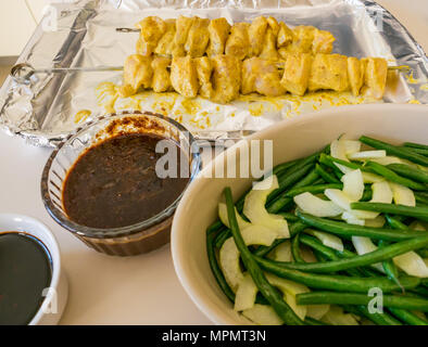 La nourriture indonésienne en préparation pour le dîner. Satay de poulet de travers sur bac déjoué, sauce aux cacahuètes, sauce kecap masin et haricots verts avec salade de concombre Banque D'Images