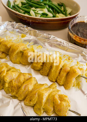 La nourriture indonésienne en préparation pour le dîner. Satay de poulet de travers sur bac déjoué prêt pour four, sauce aux arachides et de haricots verts avec salade de concombre Banque D'Images