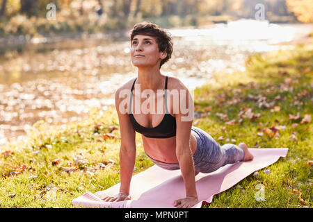 Mid adult woman in forest pratiquant le yoga, posture du cobra Banque D'Images