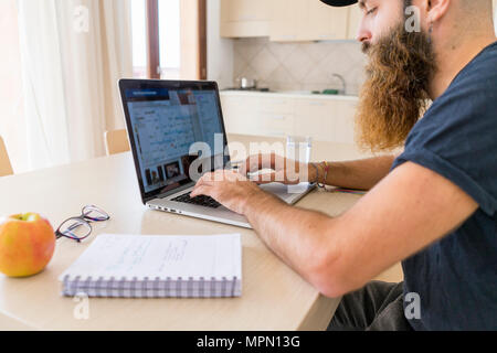 Jeune homme barbu working on laptop at home Banque D'Images