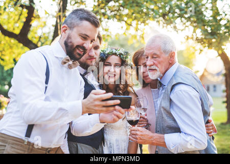 Mariée, le marié et les invités avec les smartphones en tenant l'extérieur selfies à réception de mariage. Banque D'Images