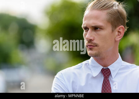 Close up of young handsome businessman thinking while looking at Banque D'Images