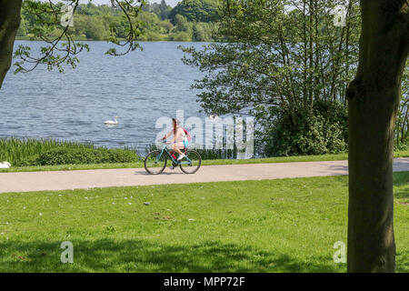 Lurgan, Irlande du Nord. 24 mai 2018. Royaume-uni - un autre très chaude journée ensoleillé à Lurgan. Une femme à vélo sur un sentier du parc à côté du lac de Lurgan Park. Crédit : David Hunter/Alamy Live News. Banque D'Images