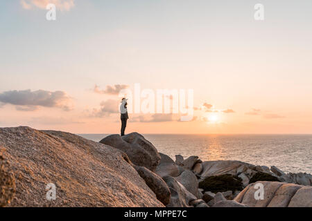 L'Italie, la Sardaigne, l'homme debout sur la roche au coucher du soleil à la vue à Banque D'Images