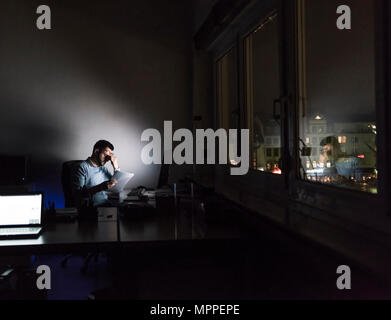 Épuisé businessman sitting at desk dans son bureau par nuit Banque D'Images