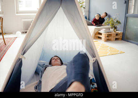Woman resting in tente , alors que le père joue avec leur fils en arrière-plan Banque D'Images