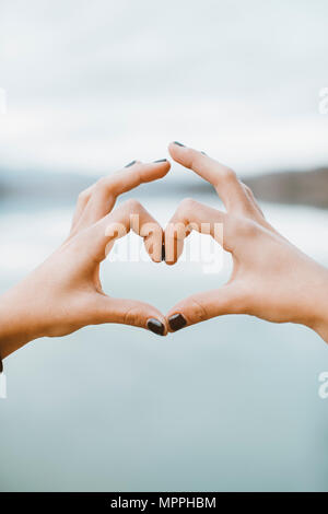 Woman's hands formant heart-shape en face du lac, close-up Banque D'Images