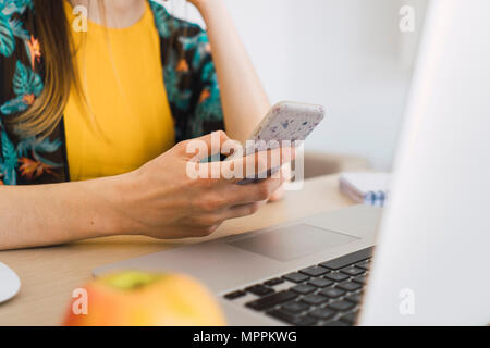 Close-up of woman sitting at table at home using cell phone Banque D'Images