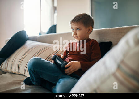 Portrait de petit garçon assis sur le canapé à jouer à jeu Banque D'Images