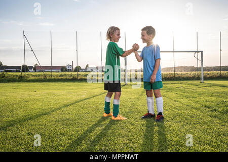 Smiling young football players shaking hands sur terrain de football Banque D'Images