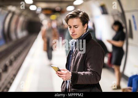 UK, Londres, homme d'affaires en attente à la station de métro using cell phone Banque D'Images