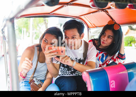 Thaïlande, Bangkok, trois amis équitation tuk tuk à prendre des photos avec le smartphone Banque D'Images