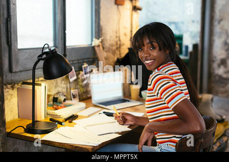 Portrait of laughing young woman sitting at desk dans un loft Banque D'Images