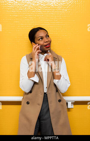 Portrait of smiling businesswoman au téléphone debout devant mur carrelé jaune Banque D'Images