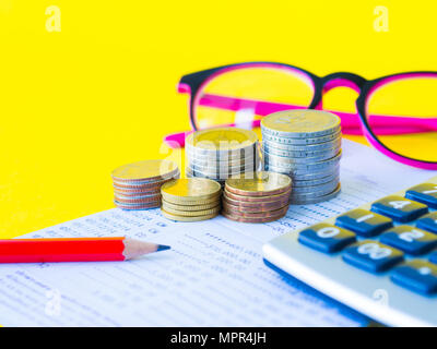 Résumé L'économie d'argent. Pile de pièces, calculatrice, lunettes roses et crayon rouge sur fond jaune Banque D'Images