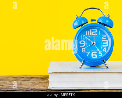 Accessoires de bureau y compris le réveil et livre blanc sur fond jaune et en bois. L'éducation et de concept d'entreprise. Banque D'Images