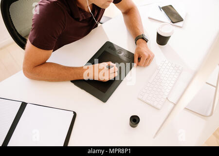 Businessman working on computer et l'aide d'un numériseur pour prendre des notes. L'homme de l'écoute audio tout en travaillant sur l'ordinateur avec un verre de café sur la table Banque D'Images
