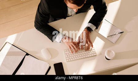 Vue de dessus d'un homme d'affaires la saisie de texte dans l'ordinateur à l'aide de clavier avec un verre de café et des documents sur la table. L'homme à l'aide d'un clavier sans fil et pe Banque D'Images