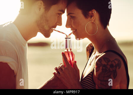 Jeune homme et femme partageant une boisson à l'extérieur. Couple drinking soft drink avec paille à partir de la même bouteille. Banque D'Images