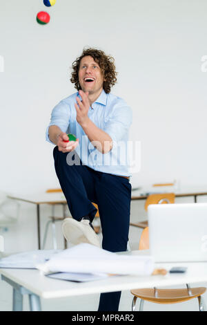 Rire businessman juggling balls dans son bureau Banque D'Images
