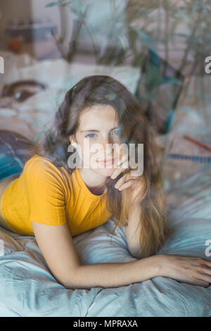 Portrait of smiling young woman lying on bed derrière la vitre Banque D'Images