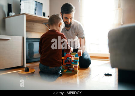 Père et fils assis sur le plancher à la maison à jouer ensemble avec des briques de bâtiment Banque D'Images