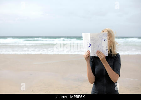 Woman covering face au livre, la lecture de poèmes sur la plage Banque D'Images