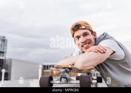 Portrait of smiling man with skateboard appuyée sur un mur Banque D'Images