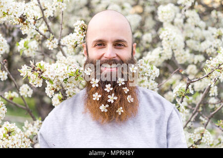 Portrait of laughing hipster avec arbre blanc fleurs dans sa barbe Banque D'Images