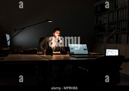 Pensive businessman sitting at desk in office at night Banque D'Images