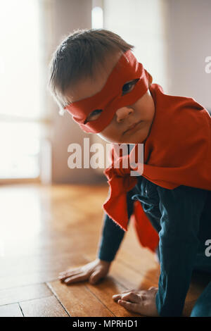 Petit garçon habillé en super héros accroupi sur le plancher à la maison Banque D'Images