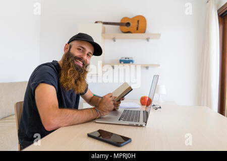 Portrait de jeune homme barbu assis à un bureau avec ordinateur portable et ordinateur portable Banque D'Images