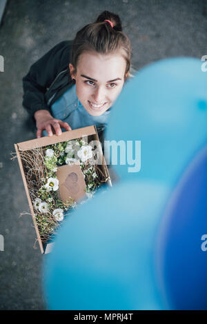 Portrait of smiling woman with présents dans boîte en carton et les ballons bleus jusqu'à Banque D'Images