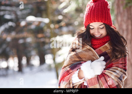 Smiling young woman wrapped in blanket in winter forest Banque D'Images