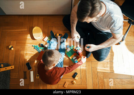 Père et fils assis sur le plancher à jouer ensemble avec des briques de construction, vue du dessus Banque D'Images