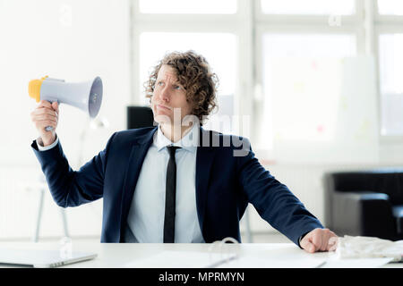 Businessman sitting in office essayer megaphone Banque D'Images