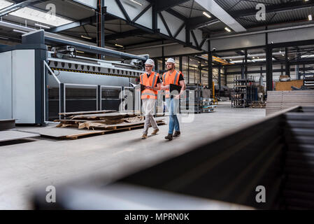 Deux hommes portant des casques et des gilets de sécurité marche sur magasin d'usine marbre Banque D'Images