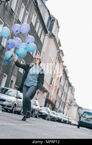 Femme heureuse avec des ballons bleu marche dans la rue Banque D'Images