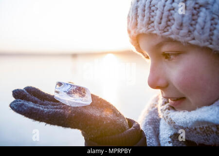 Allemagne, Brandebourg, lac Straussee, portrait d'une jeune fille debout sur lac gelé, à la recherche de bloc de glace sur sa main Banque D'Images