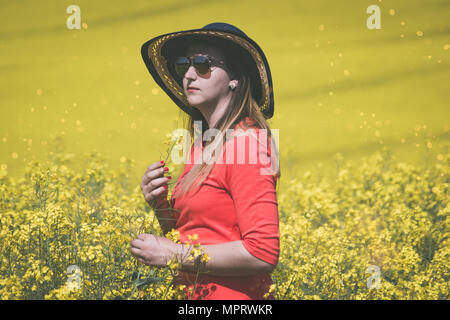 Une jeune femme portant une robe rouge dans les champs jaunes de colza. Banque D'Images