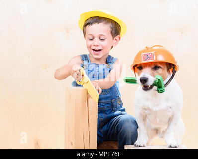 Kid et dog wearing hardhats travailler avec scie et marteau at construction site Banque D'Images