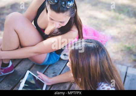 Couple de jeunes femmes de la génération y assis dans pinède à l'aide de tablet - social dépendant, phubbing, technologie concept Banque D'Images