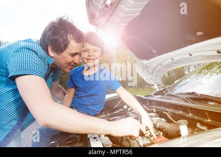 Portrait de jeune père de la réparation du moteur pendant que son petit garçon assis sur le capot de la voiture ouvert cassé Banque D'Images