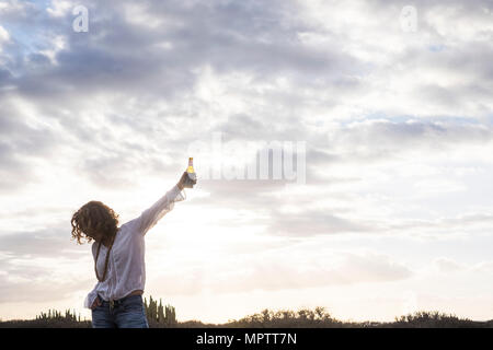 Beau et mignon 40 ans vieux modèle femelle avec de la bière à la main. rock'n roll poser pour la réussite et l'humeur. concept gagnant désert et nuages ciel dans le dos Banque D'Images