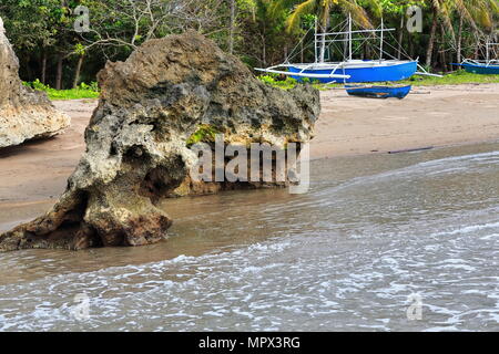 Les affleurements rocheux de calcaire très érodé dans le sable marquant l'extrémité sud de la plage et des bateaux. échoués sur bangka bleu Nauhang-barangay Sipal Banque D'Images